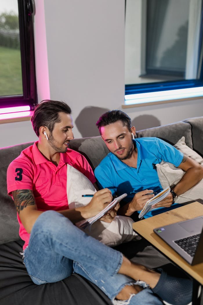 Two brothers studying together on a couch with notebooks and a laptop.